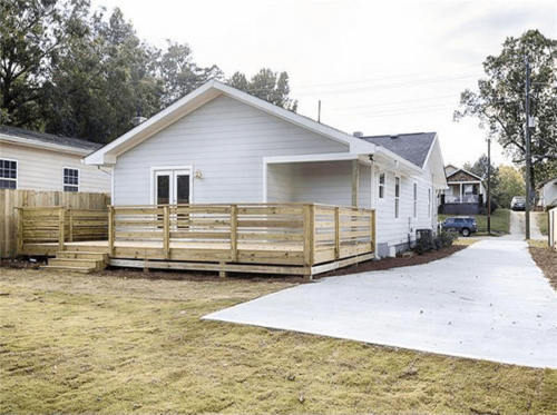 Back of house with wooden porch, driveway and grass