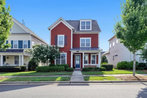 Street view of a 2-story red home with white trim in neighborhood