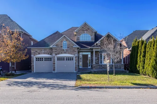 Streetview of a 2-story brick home with a 2-car garage and trees on either side