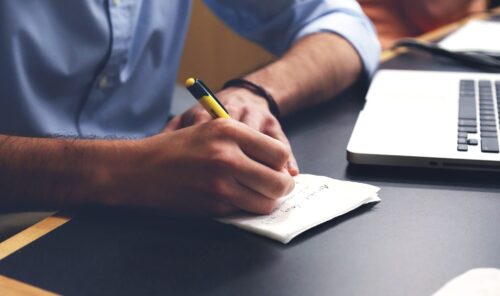 Man writing on napkin with laptop nearby