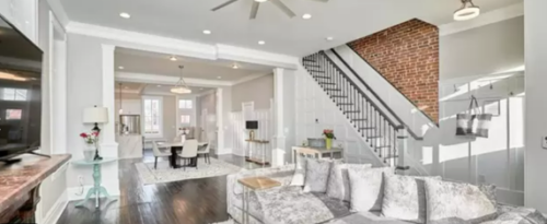 An shot of an all white living room with exposed brick in the background and a tv in the foreground