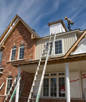 Ladder laying against two story house with construction worker working on chimney