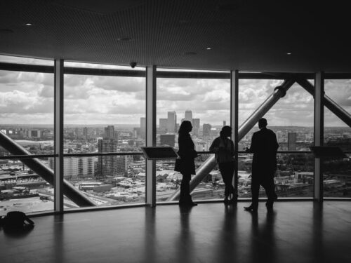 Three people at a networking event discussing real estate standing in front of large windows with the cityscape in the background.