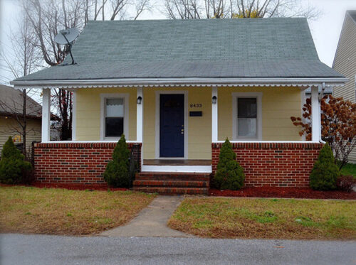 Small yellow house with awning covering front porch and brick frame