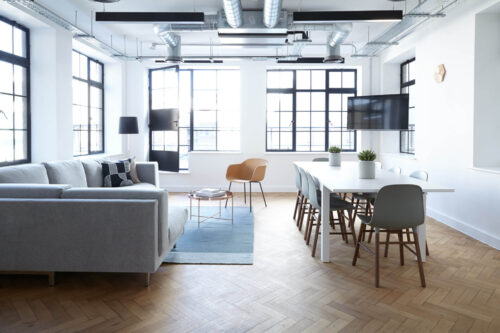 Modern office and conference room with large windows, couch, table, and flat screen mounted on wall